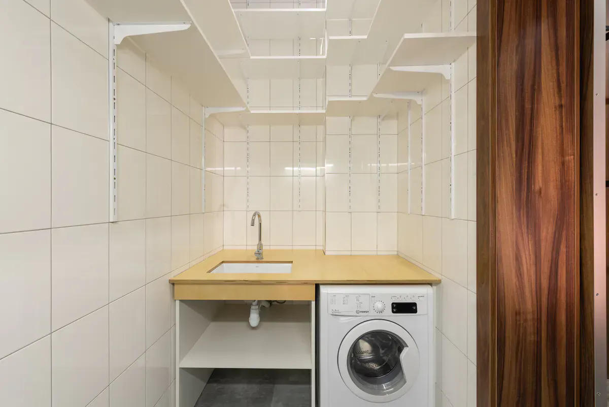 Compact laundry closet with a washing machine and open shelving, the tight footprint that crushes ordinary vent hose