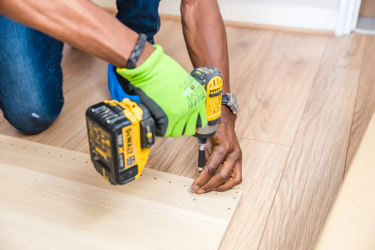 Gloved hands working a cordless drill indoors, the slow and steady technique that frees a stuck dryer vent brush