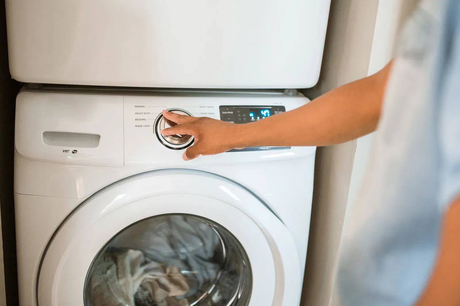 Hand turning the cycle dial on a stacked washer and dryer, the first check when a dryer smells like burning