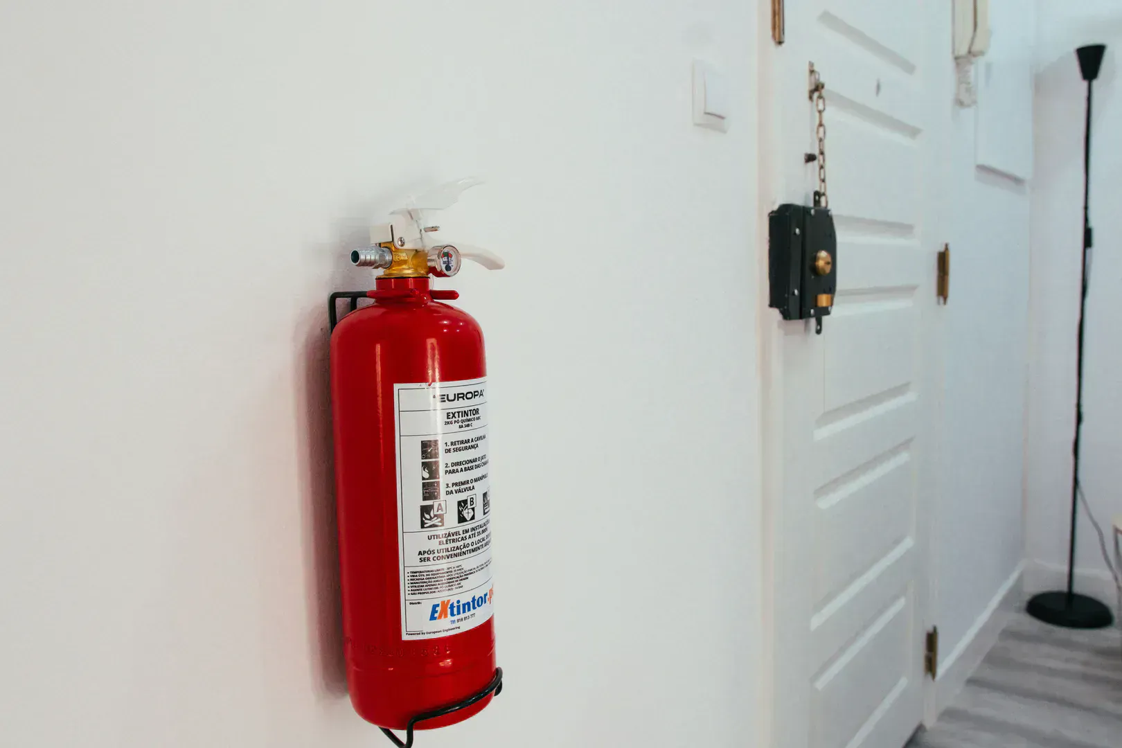 Red fire extinguisher mounted on a white wall in a home hallway between the kitchen and garage