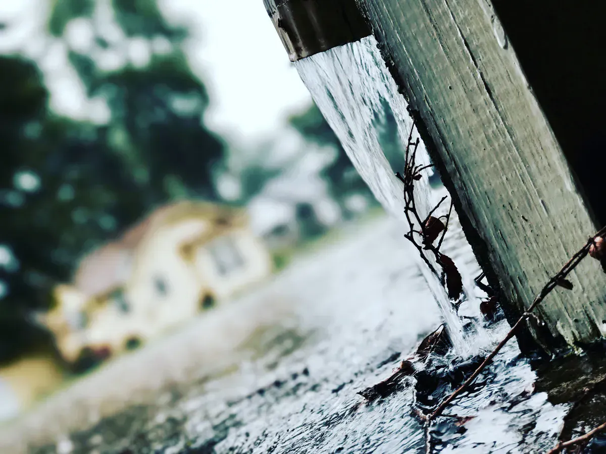 Rainwater pouring over the edge of a clogged gutter during a storm, the classic sign it is time to clean