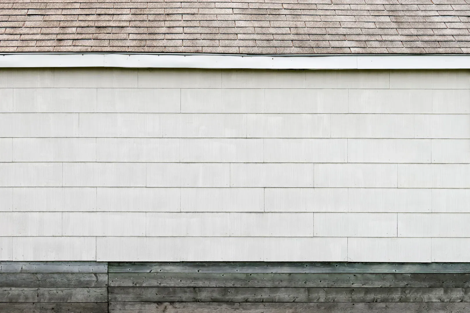 White lap siding and a shingled roofline, the exterior wall where a 4-inch dryer vent cover mounts