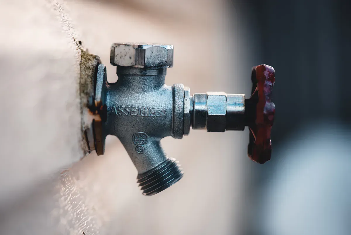Bare metal hose bib mounted on an exterior wall, uncovered and exposed ahead of the first freeze