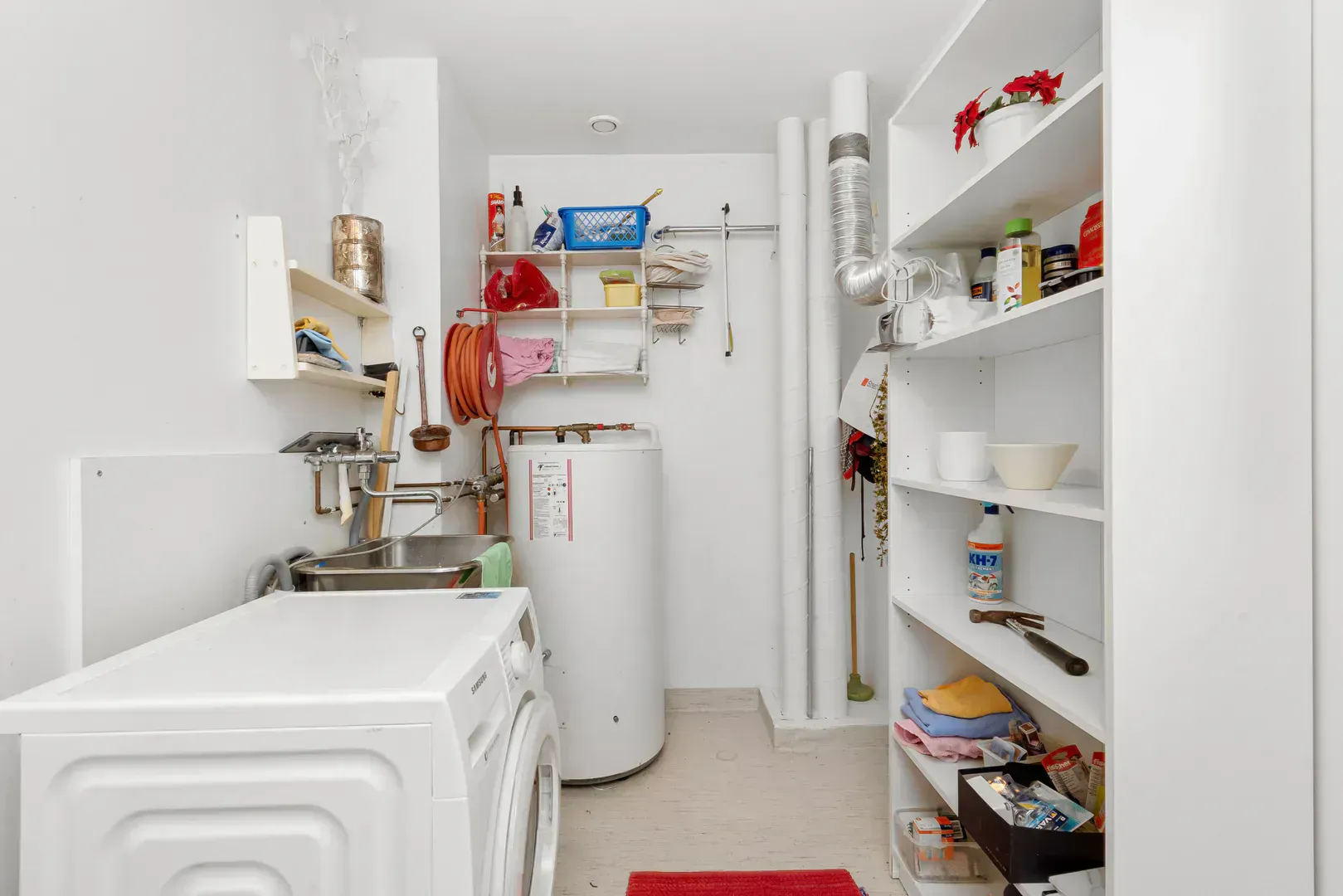 Tank water heater standing beside the washer in an organized home laundry and utility room