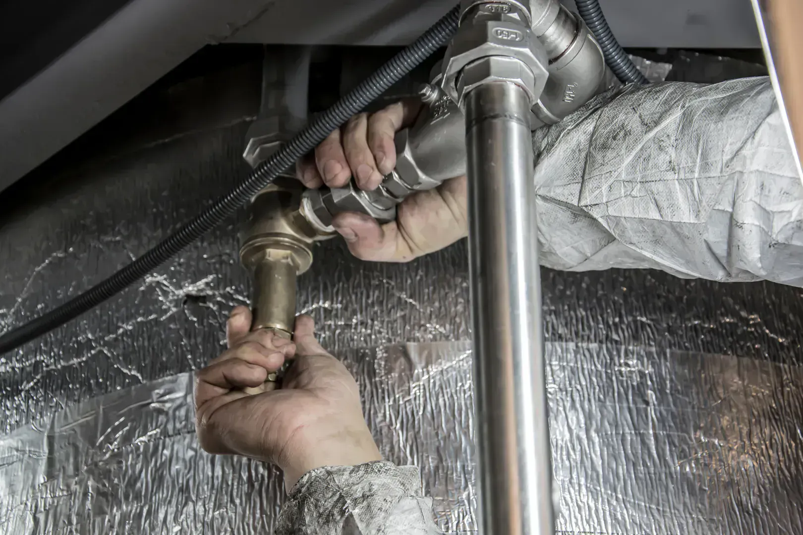 Hands adjusting home water pipes with pliers during a plumbing maintenance job