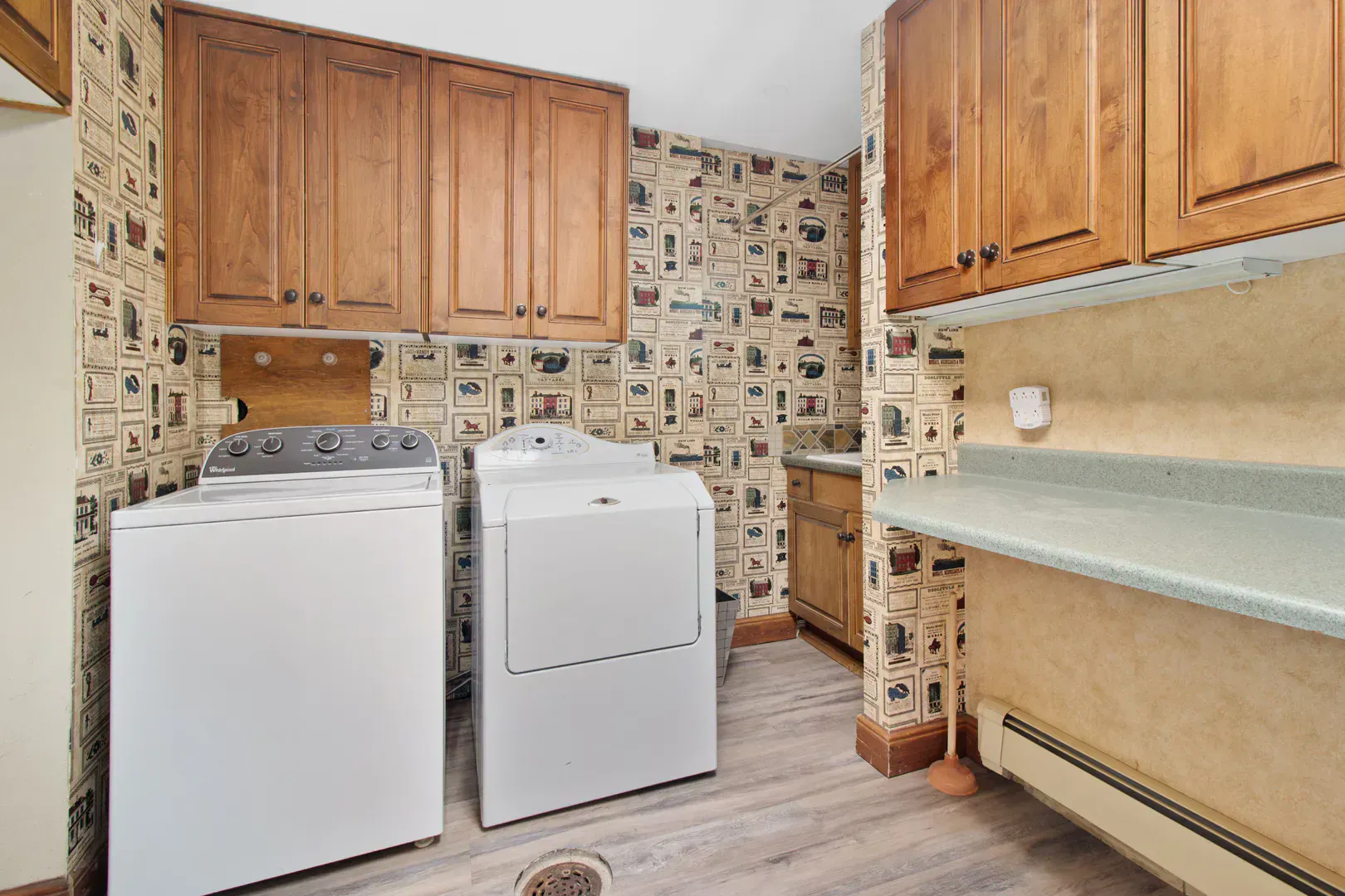 Laundry room with wooden cabinets and a washer and dryer pair that hide supply hoses and a drain pan behind them
